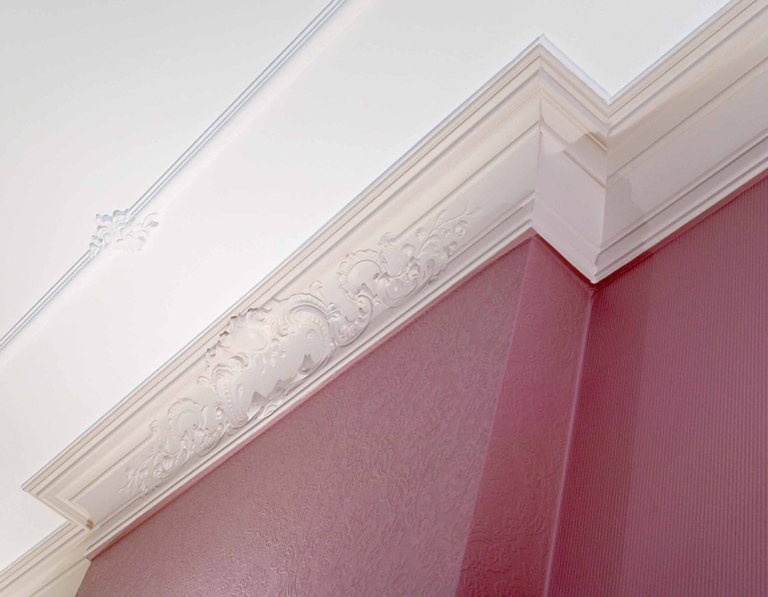 Das Bild zeigt eine weiße Decke mit Stuck, der bis an die rote Wand reicht